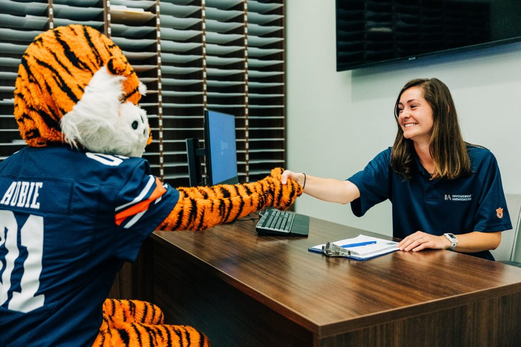 An Involvement Ambassador shaking Aubie the Tigers hand over a desk