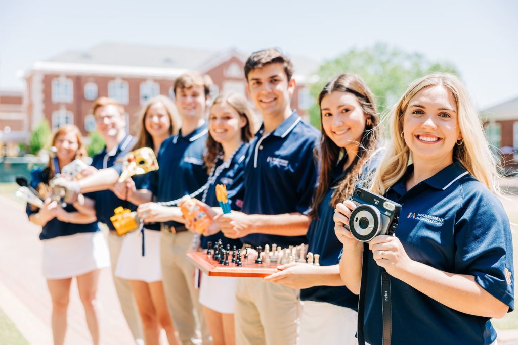 Students standing in a line holding different objects that represent organizations on campus. 